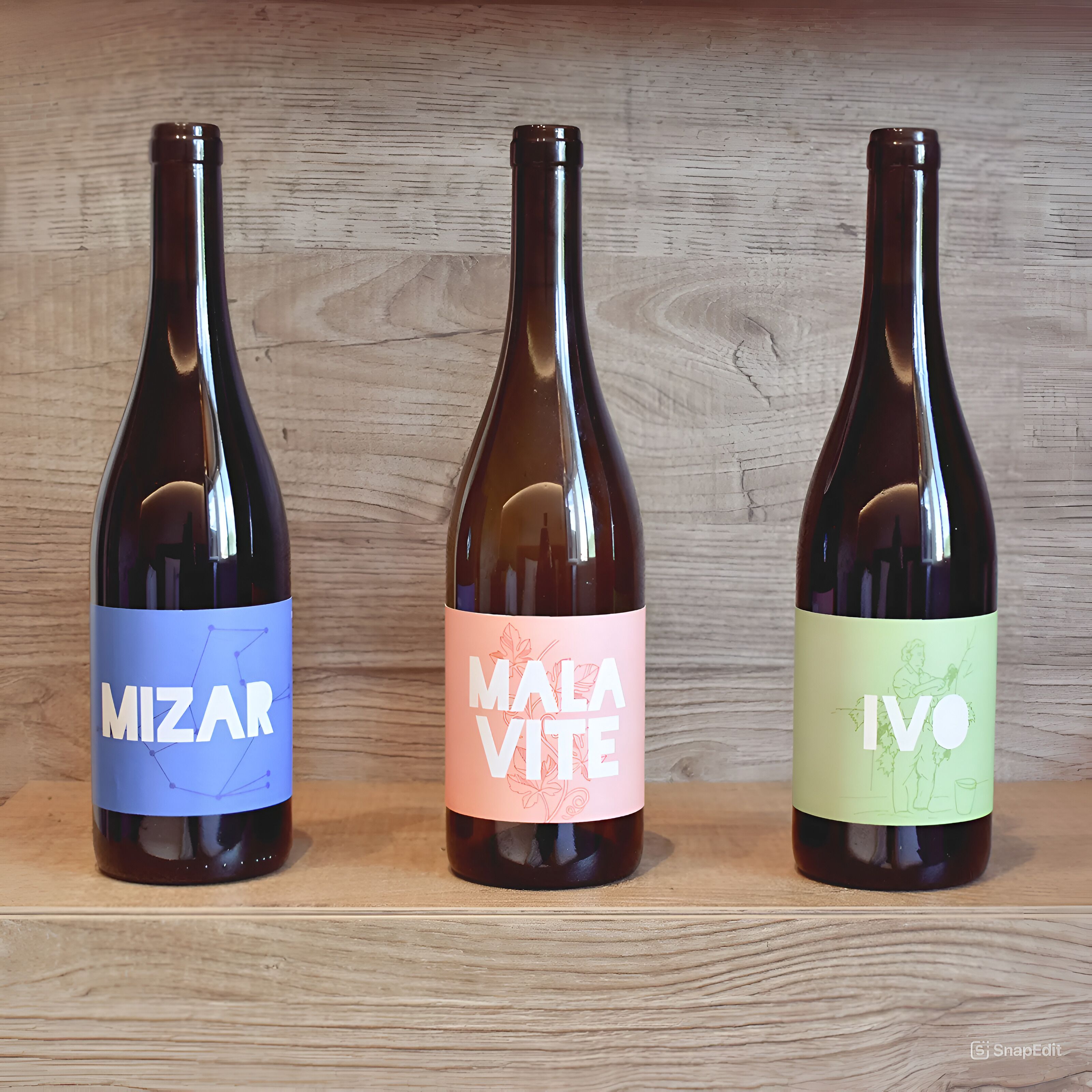 Tres botellas de vino con etiquetas sobre una repisa de madera.