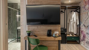 Ein modernes Zimmer mit einem Holztisch, einem grünen Stuhl, einem Flachbildfernseher, einer Kaffeemaschine und einer kleinen Pflanze.
