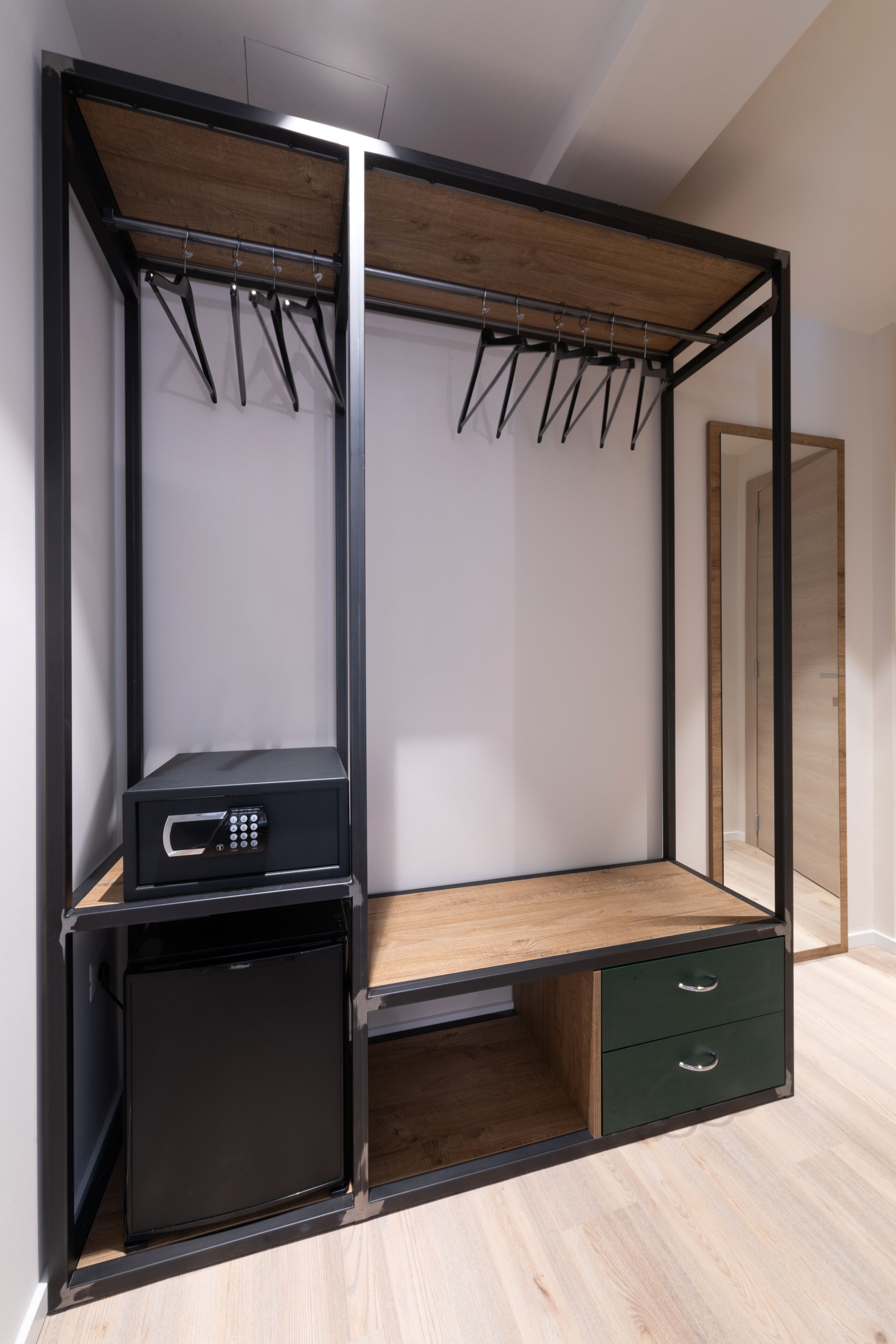 Ein begehbarer Kleiderschrank mit einem Spiegelkleiderschrank, ein kleiner, schwarzer Kühlschrank und ein Holztisch mit Schubladen.