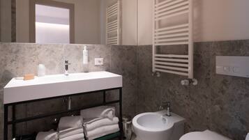 A modern bathroom with a large mirror, a vanity with a sink, a bidet, and a toilet.