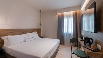 A hotel room with a large bed, a desk with a chair, a television, and a window with curtains.