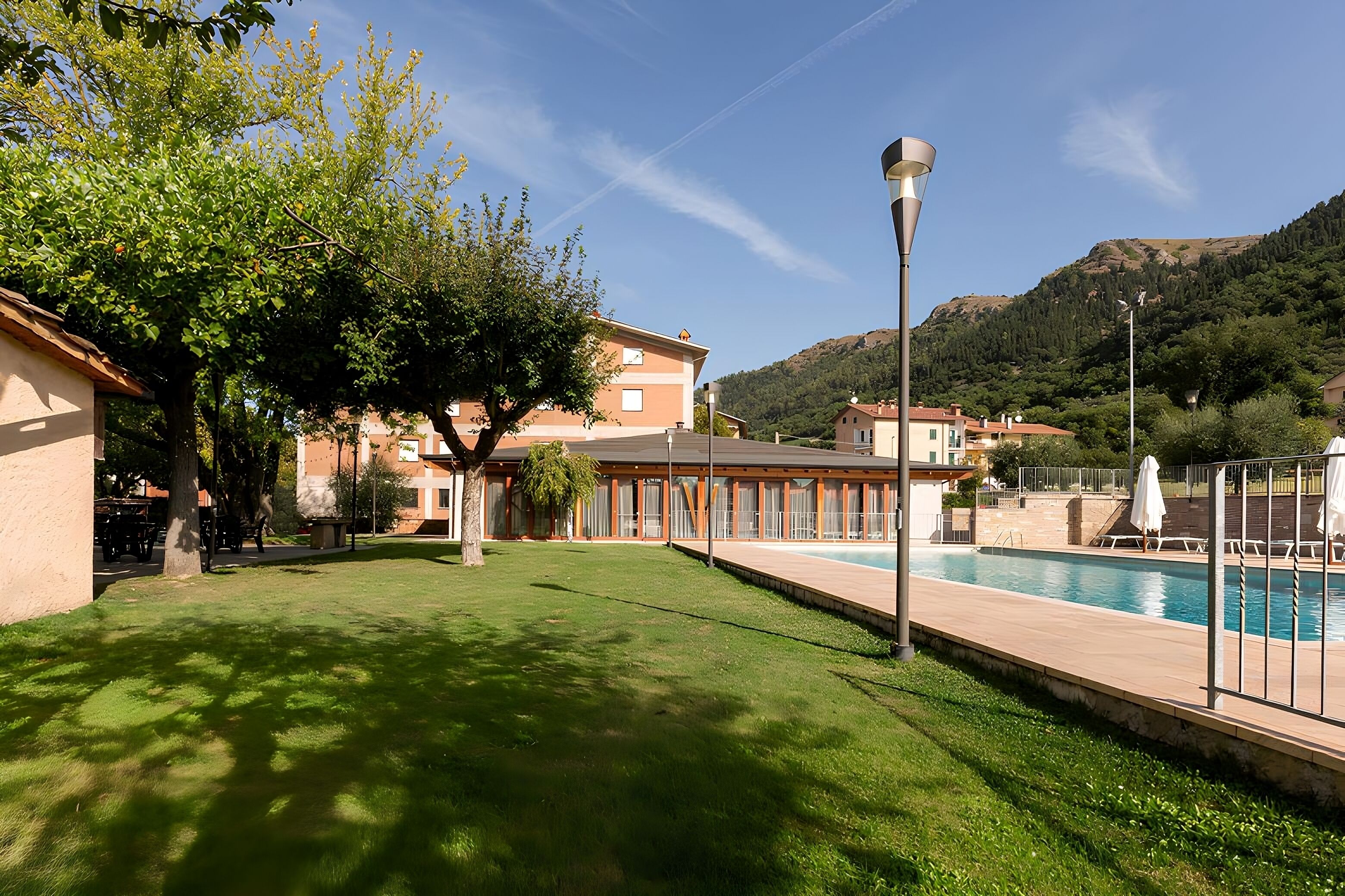 Zona de piscina con vista despejada a la piscina, un farol y un edificio con techo rojo al fondo.