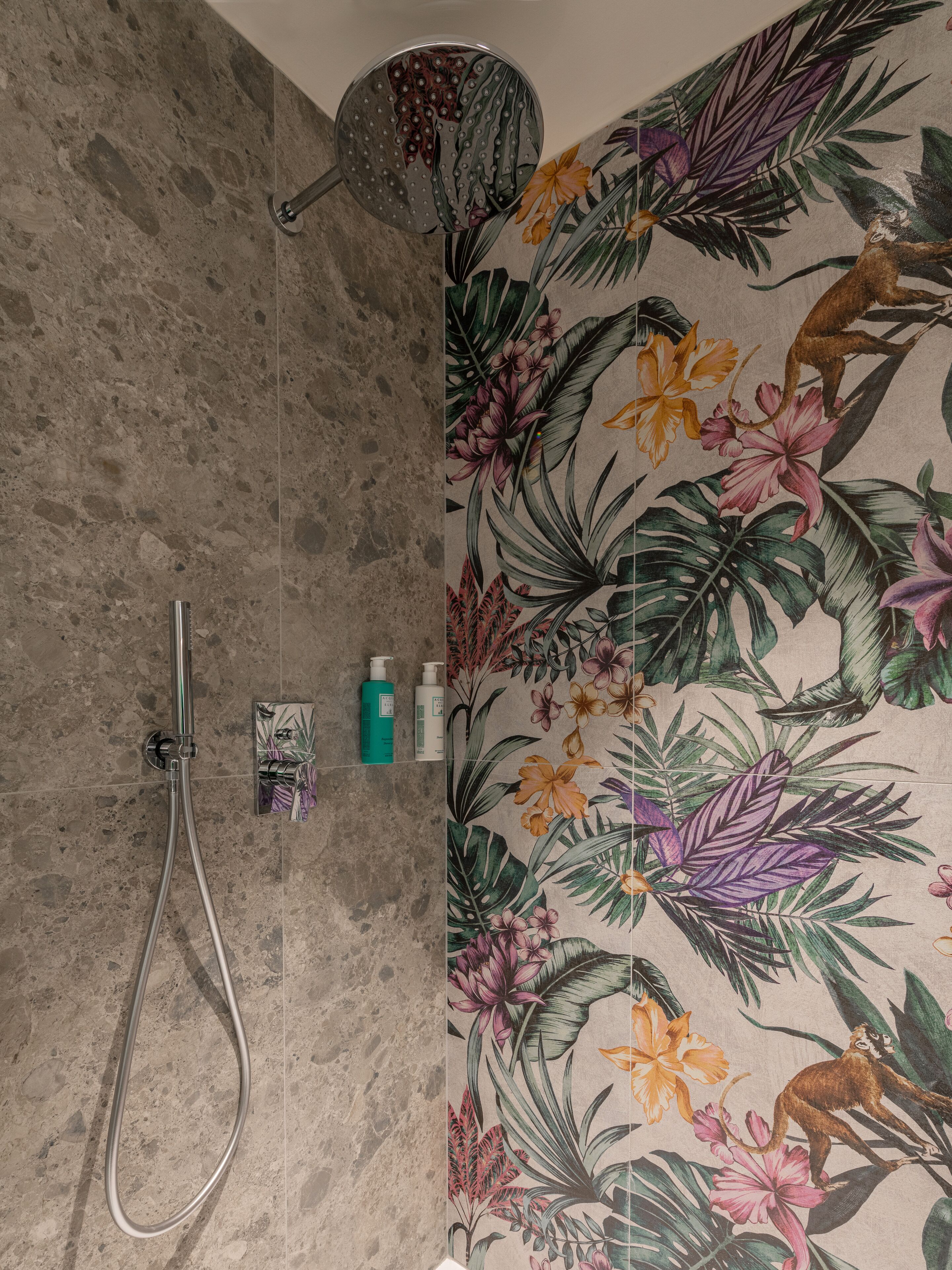 Una doccia con soffione a mano, pannello di controllo a parete e una selezione di articoli da toilette su uno scaffale.