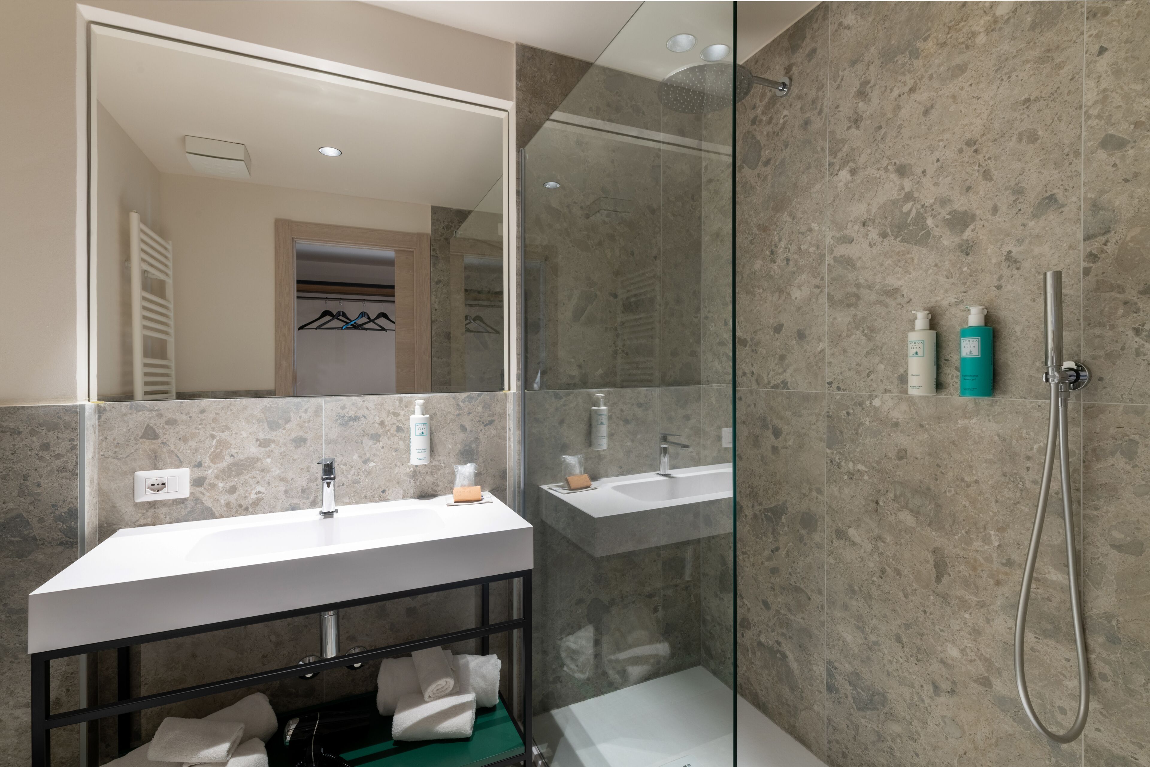 A modern bathroom with a glass-enclosed shower, a vanity with a mirror, and toiletries on the wall.