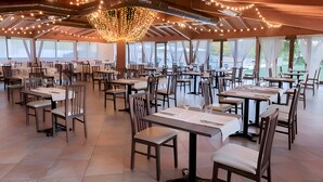 A spacious dining area with multiple tables and chairs, large windows, and a decorative chandelier. - Catignano Hotel (Gubbio)
