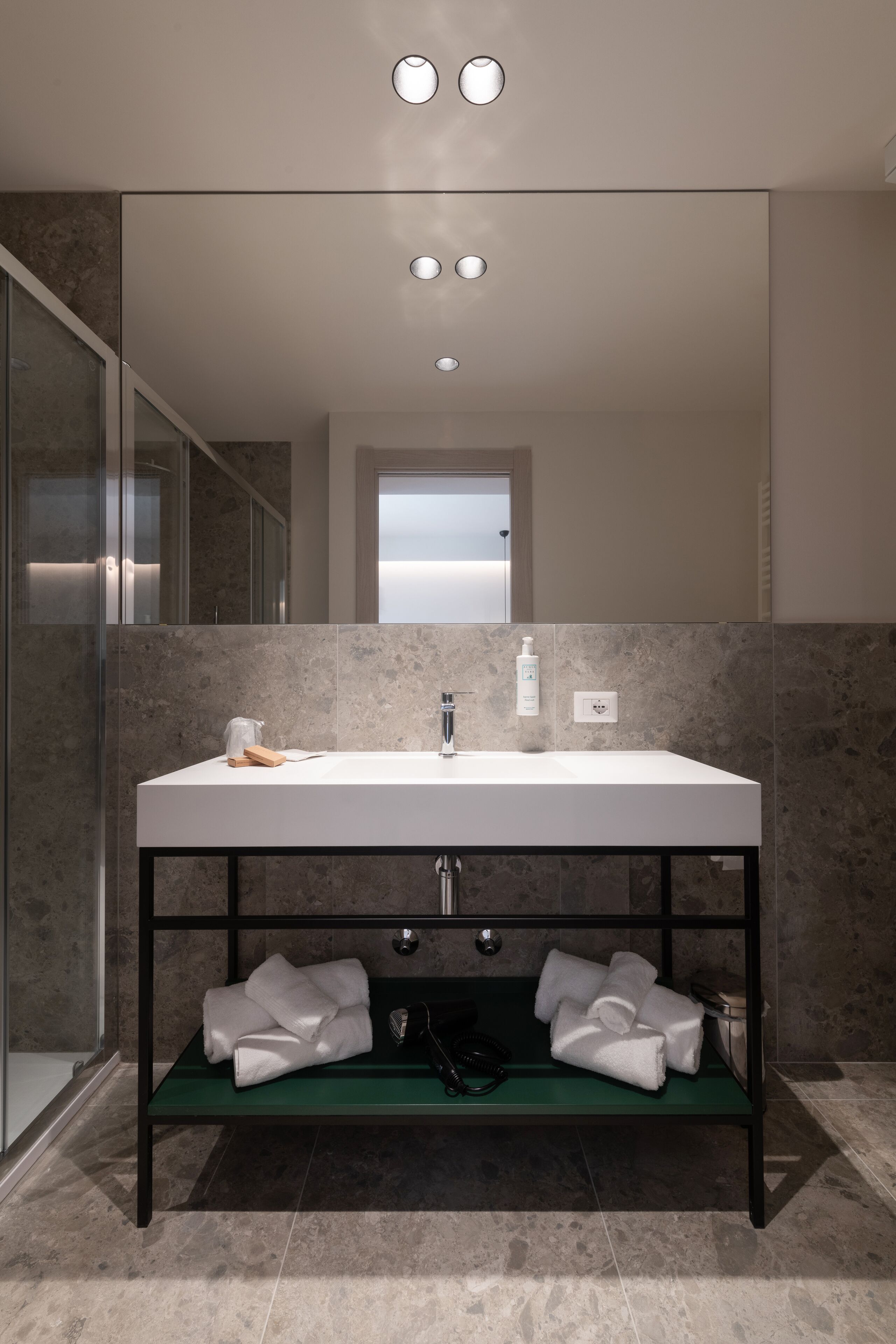 Un baño moderno con un espejo grande, un lavamanos blanco y un estante con toallas.