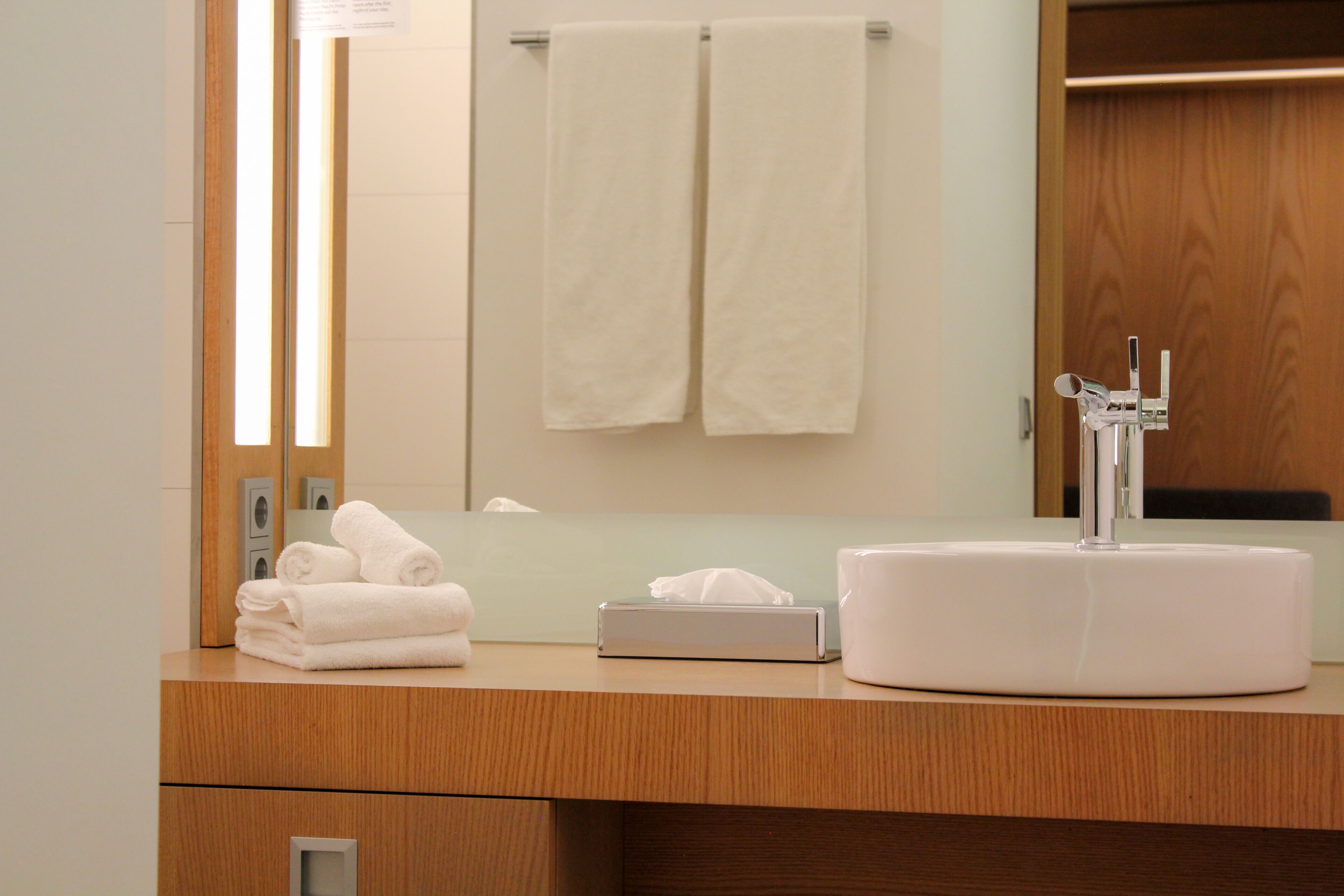 A bathroom with a wooden vanity, a white sink, and two towels hanging on the wall.