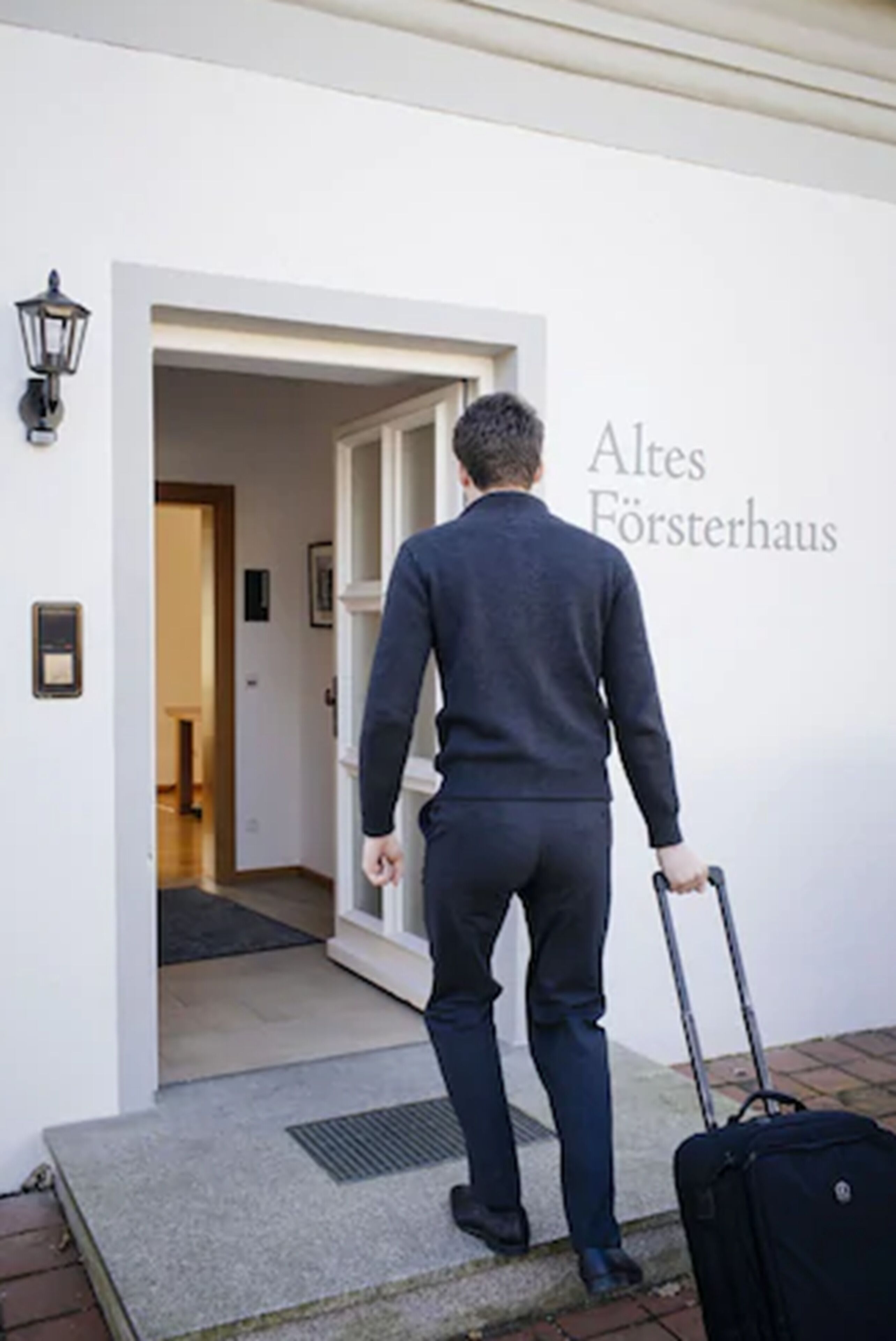 A man in a dark suit walking towards a door labeled "Altes Försterhaus."
