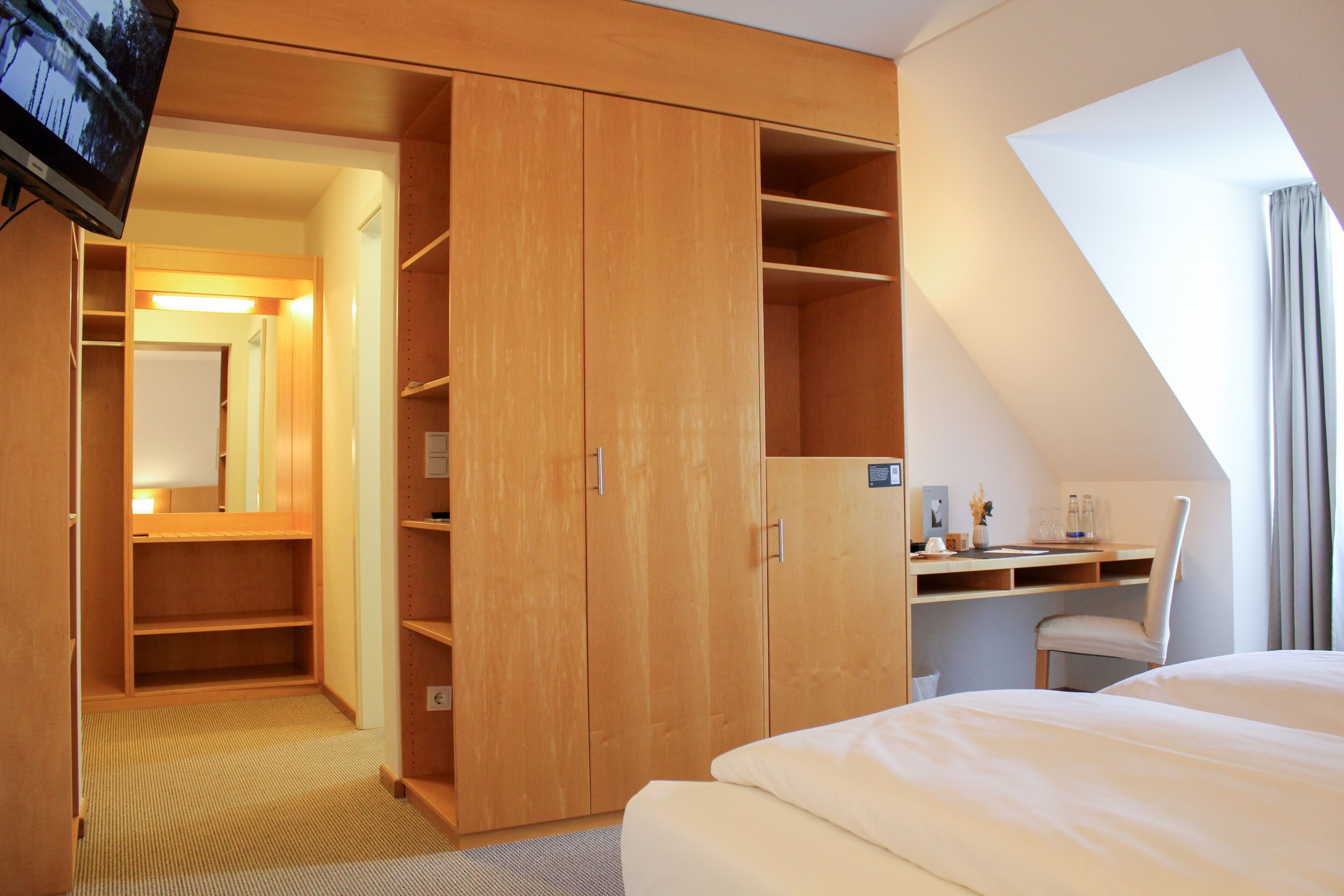 A hotel room with a large wardrobe, a desk with a chair, and a bed.