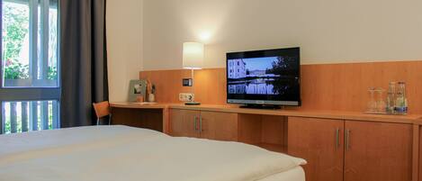 Una habitación de hotel con una cama, televisión, escritorio, silla y ventana con cortinas.