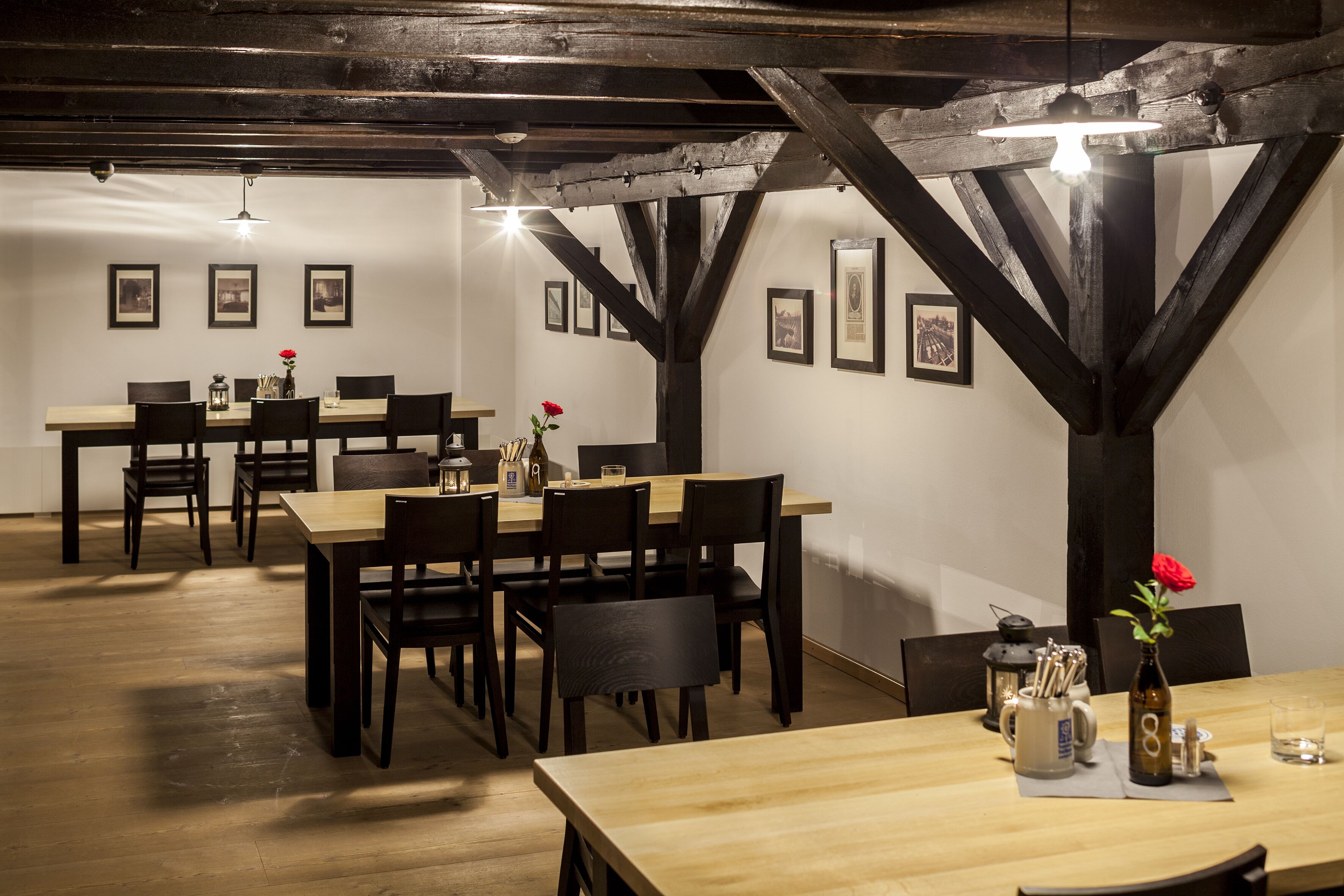 A dining area with wooden tables and chairs, framed pictures on the walls, and a rustic ceiling with exposed beams.