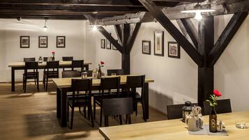 A dining area with wooden tables and chairs, framed pictures on the walls, and a rustic ceiling with exposed beams.