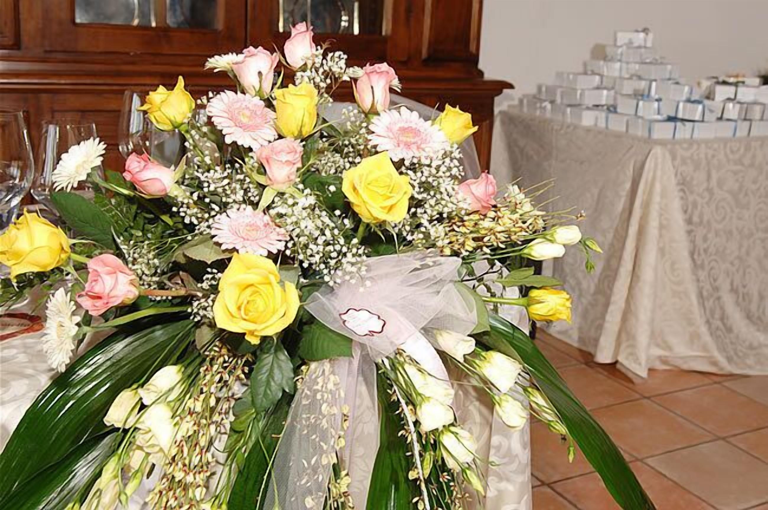 A bouquet of flowers with yellow and pink roses, white daisies, and baby's breath, placed on a table.
