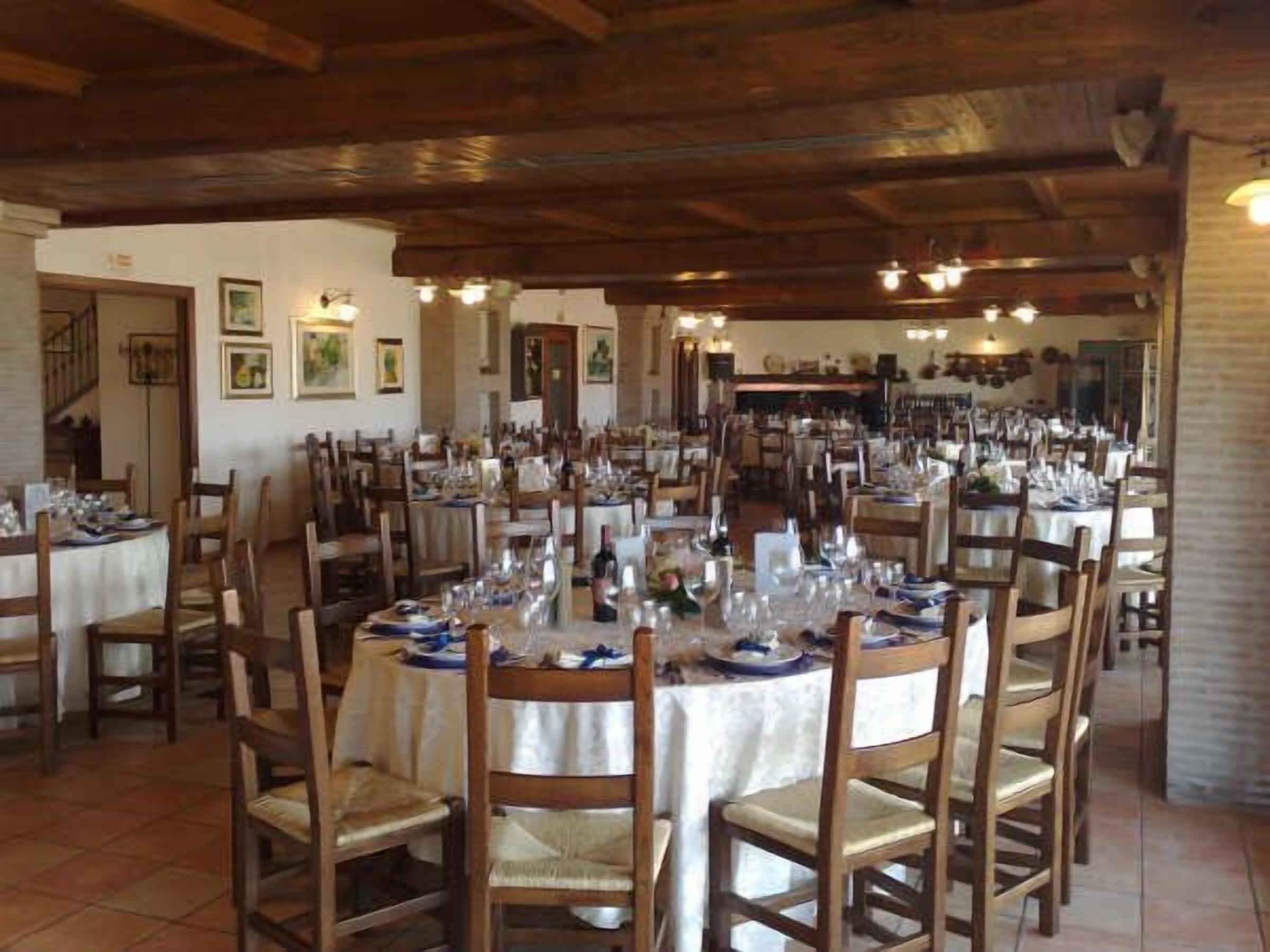 A restaurant with multiple round tables, wooden chairs, and a rustic interior with exposed wooden beams and tiled floors.