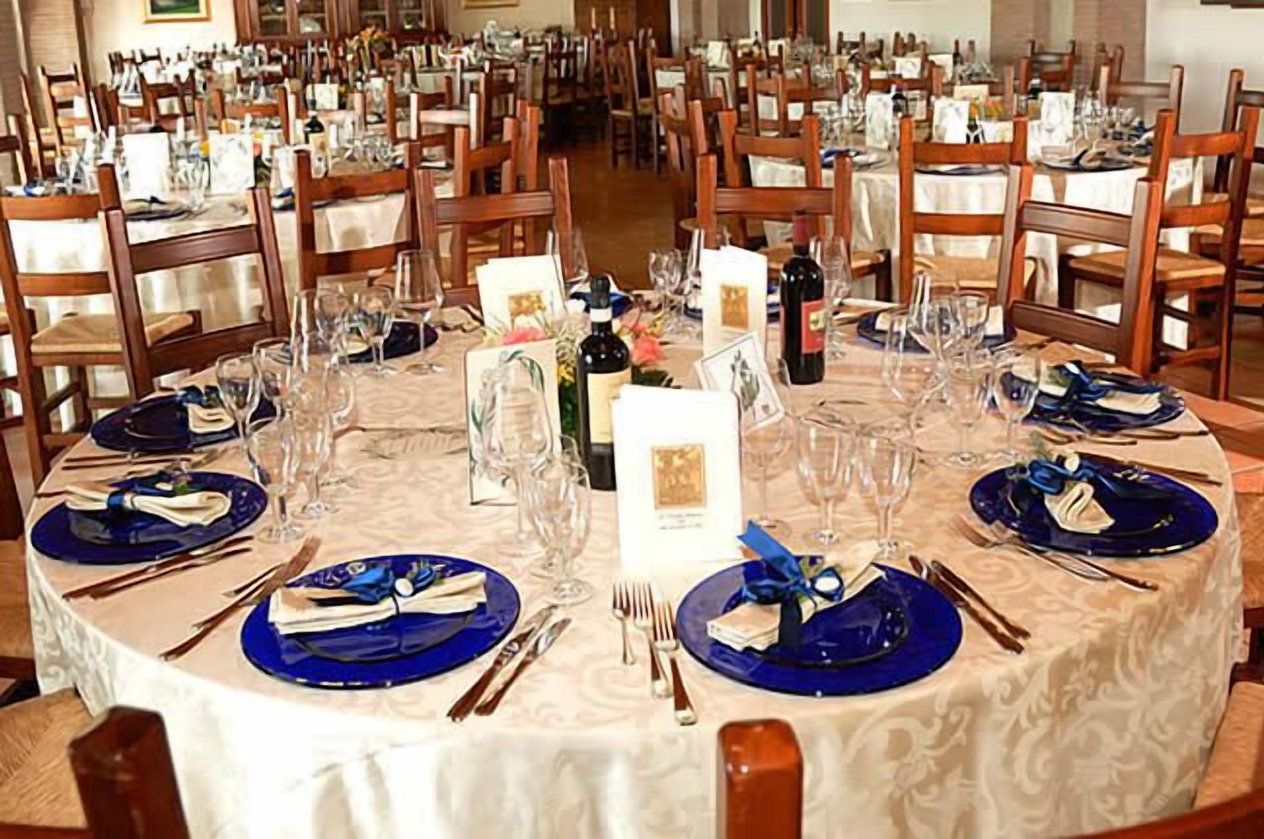 Een feestzaal met ronde tafels gedekt voor een formeel evenement, met blauwe tafelkleden en witte servies.