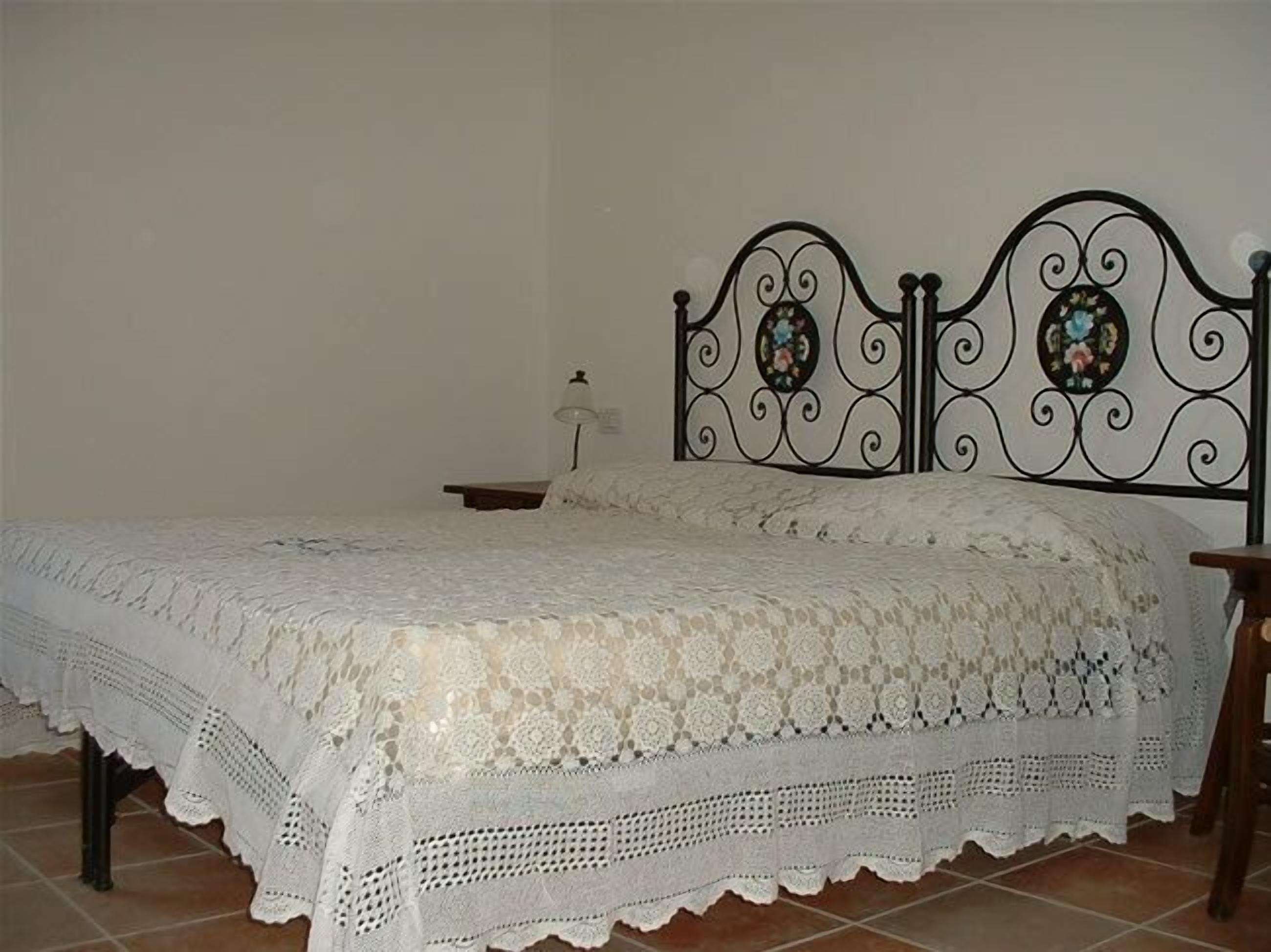 Una cama con una colcha blanca de encaje y un cabecero de metal con detalles decorativos.
