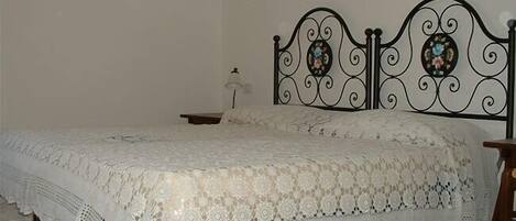 Una cama con una colcha blanca de encaje y un cabecero de metal con detalles decorativos.