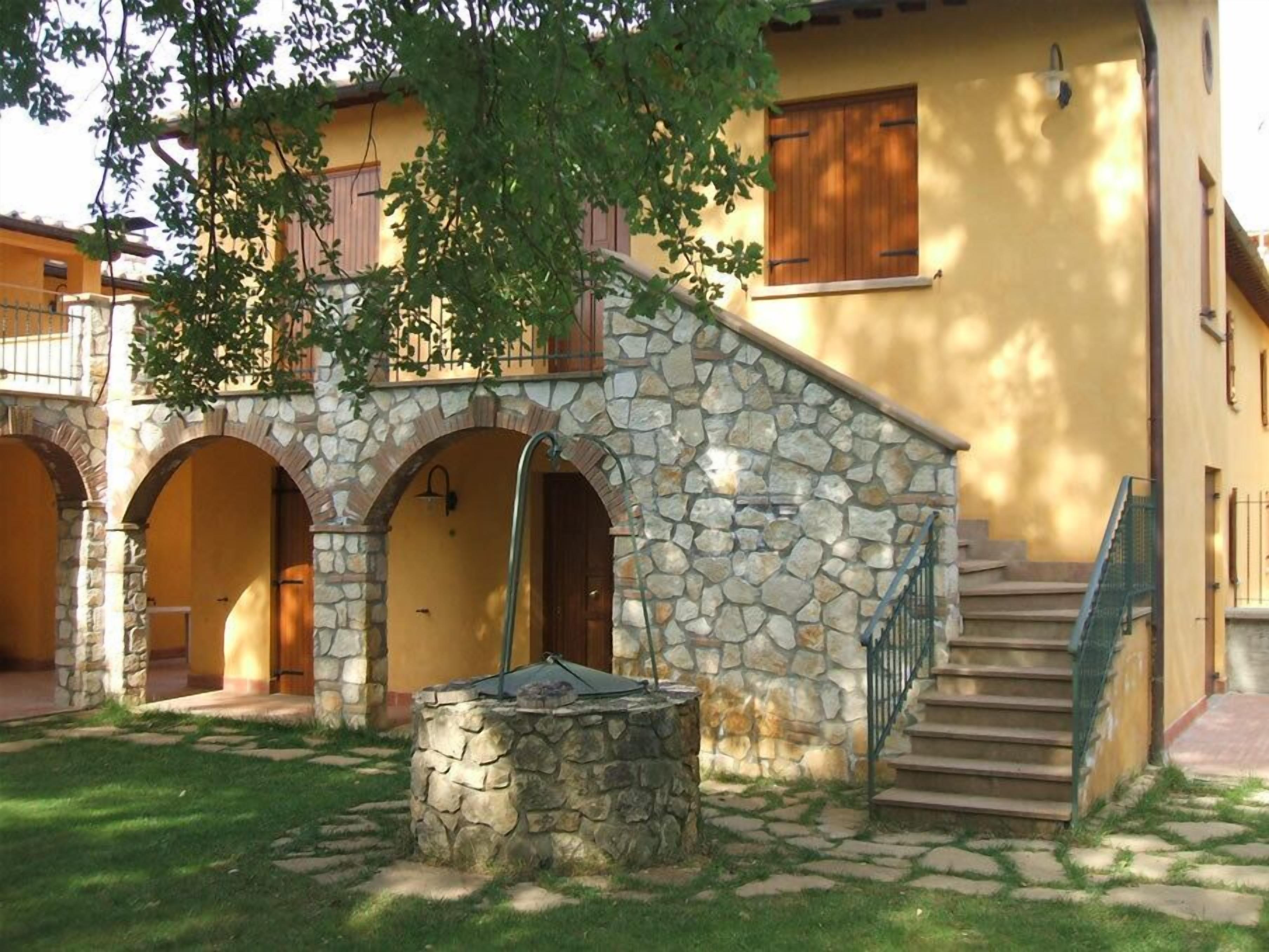 Ein Innenhof mit einem Steinfountain, einer Holztreppe und einem Gebäude mit Rundbogenöffnungen.