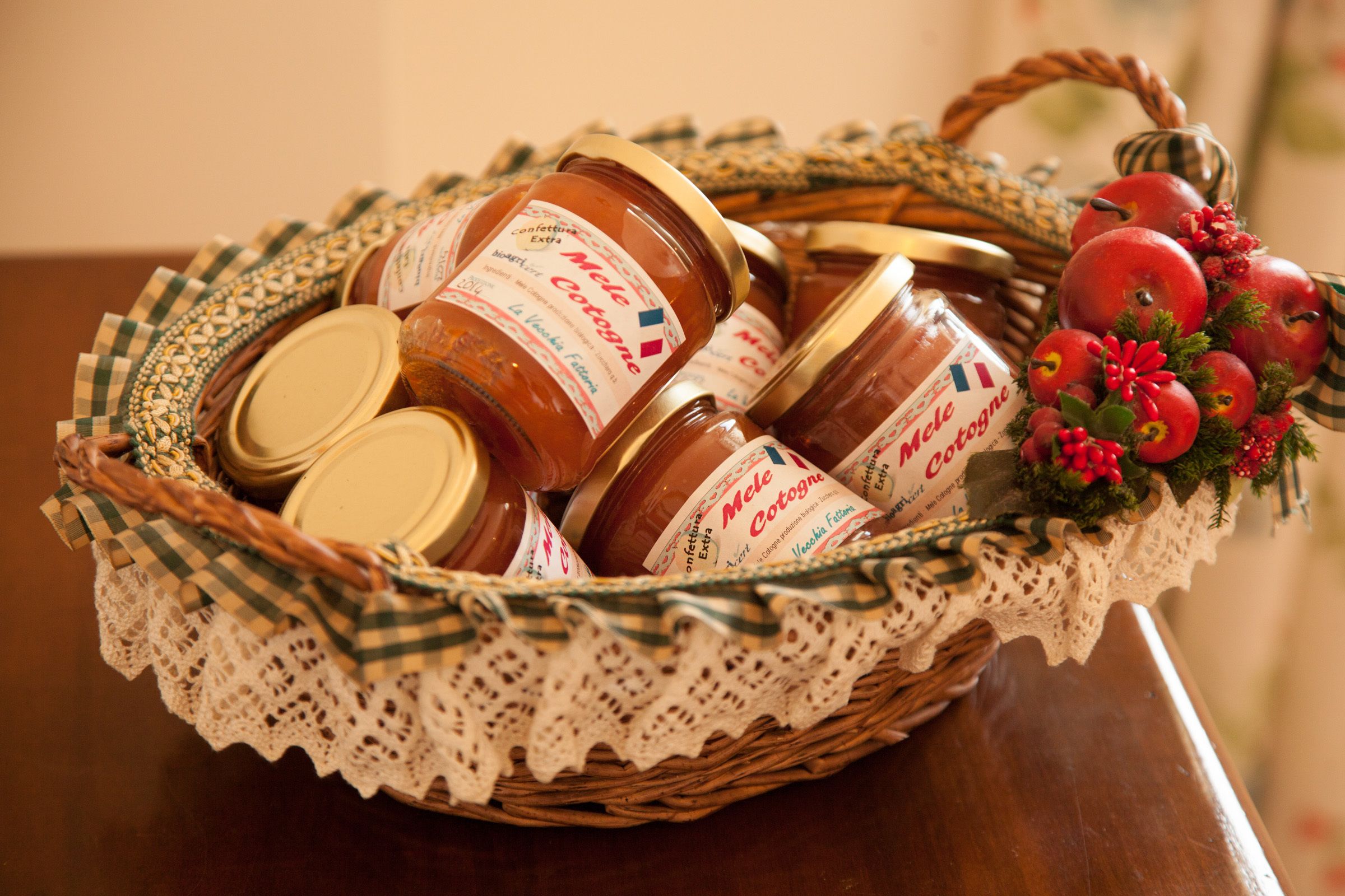 A wicker basket filled with jars of honey and decorated with red apples and greenery.