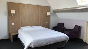 A bedroom with a bed, a nightstand, two chairs, a skylight, and a wooden headboard.