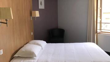 Habitación de hotel con una cama, una silla, un escritorio con teléfono y una ventana con cortinas.
