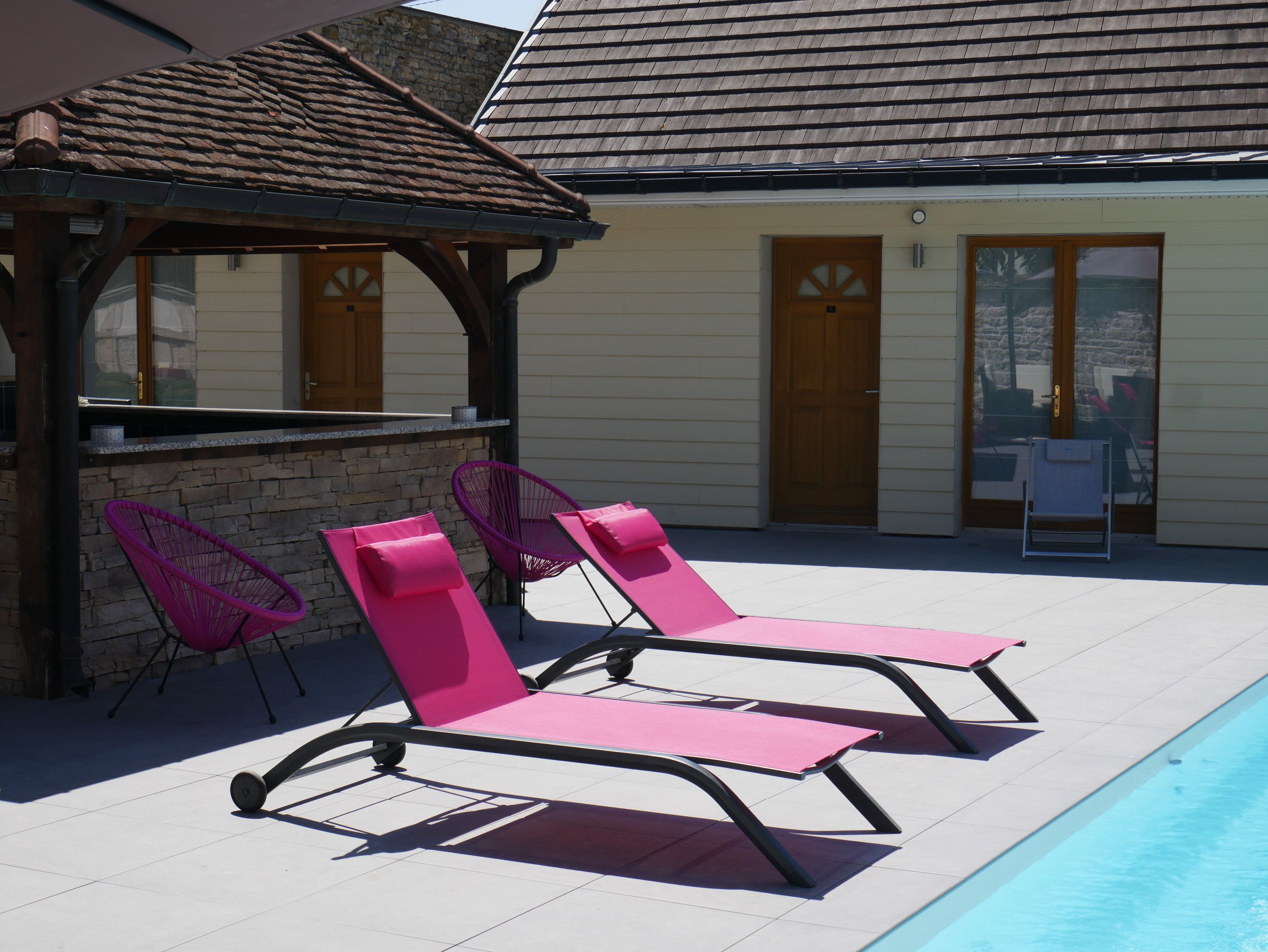 Un espace aménagé au bord de la piscine, avec deux chaises longues roses, un petit coin bar et un mur en pierre.
