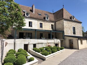 A stone building with a courtyard, featuring a covered walkway, potted plants, and a well-maintained garden. - L'hôtel d'Arc (Arc-sur-Tille)