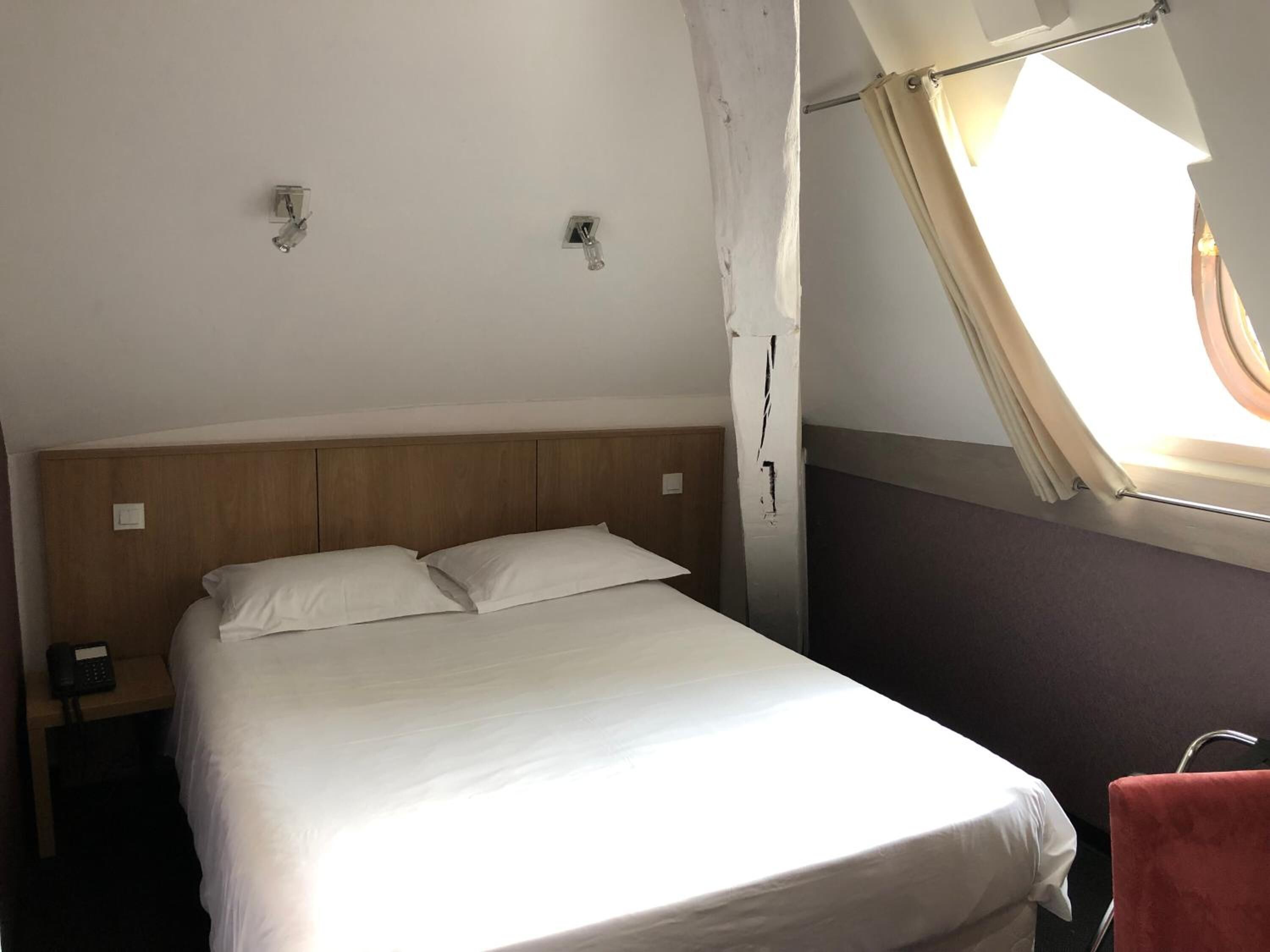 Een enkel bed met houten hoofdbord, een bedtafeltelefoon en een raam met gordijnen.