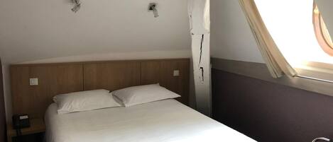 Una cama individual con cabecera de madera, teléfono en la mesita de noche y ventana con cortinas.