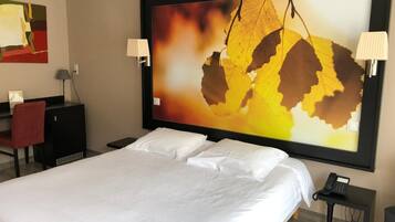 Habitación de hotel con una cama grande, dos mesitas de noche, un escritorio con una silla y un cuadro abstracto de gran tamaño en la pared.