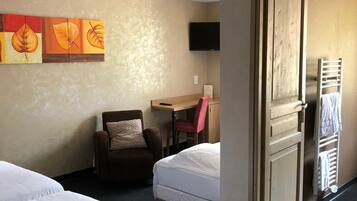 A hotel room with two beds, a desk, a chair, a TV, and artwork on the wall.