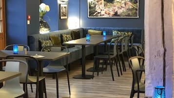 Un restaurant au décor moderne, proposant différents types de sièges, notamment des tables et un canapé. On y trouve également des éléments décoratifs, comme un vase avec des fleurs et un grand tableau au mur.