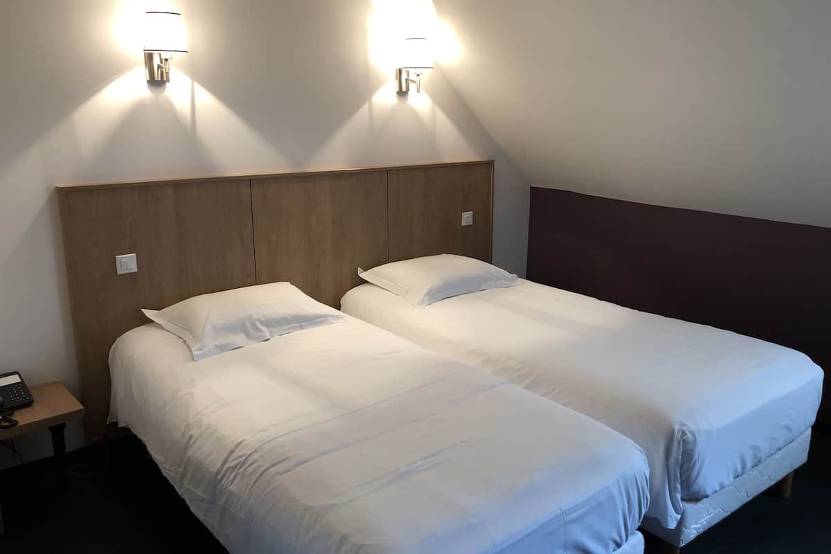 A hotel room with two single beds, wooden headboards, and wall-mounted lights.