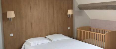 A bedroom with a wooden headboard, two bedside lamps, a crib, and a small bedside table.