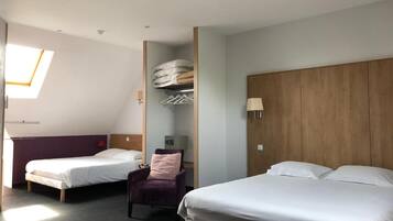 A hotel room with two beds, a chair, a wardrobe, and a skylight.