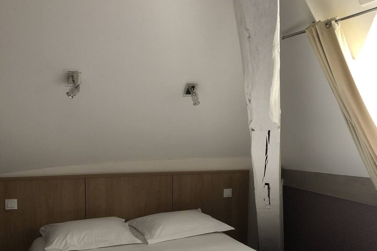 A bed with white linens in a room with a sloped ceiling and wooden headboard.