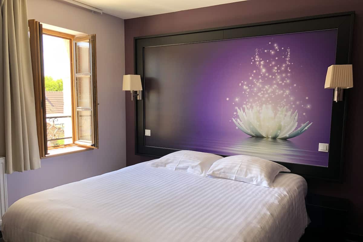 A hotel room with a bed, a large wall-mounted TV, and two bedside lamps.