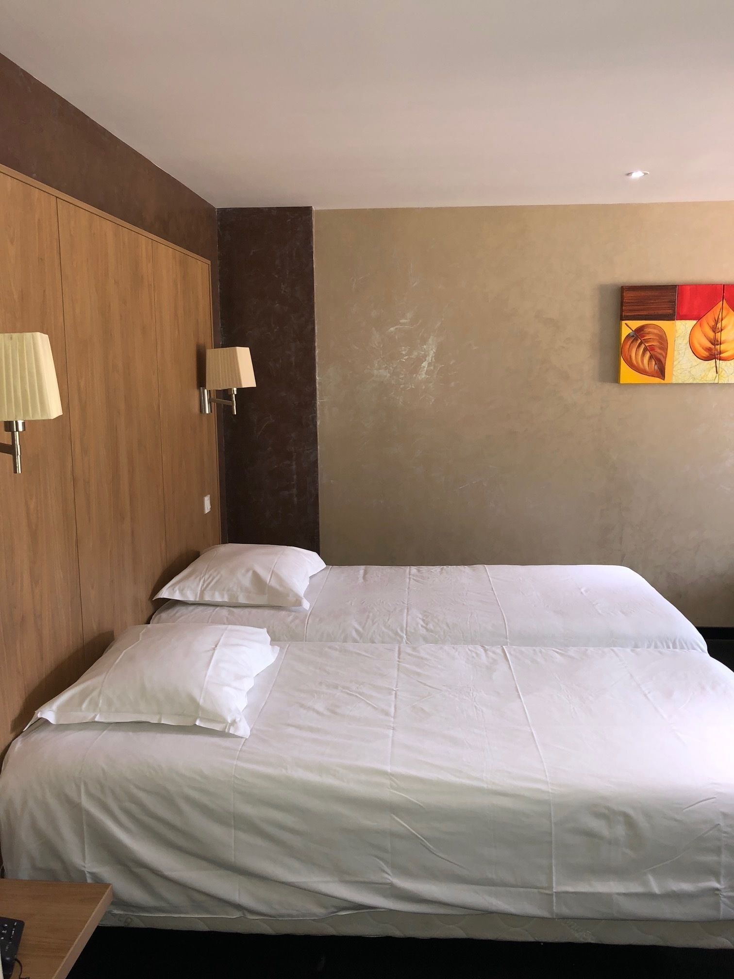 A hotel room with a large bed, two bedside lamps, a wooden headboard, and a wall painting.