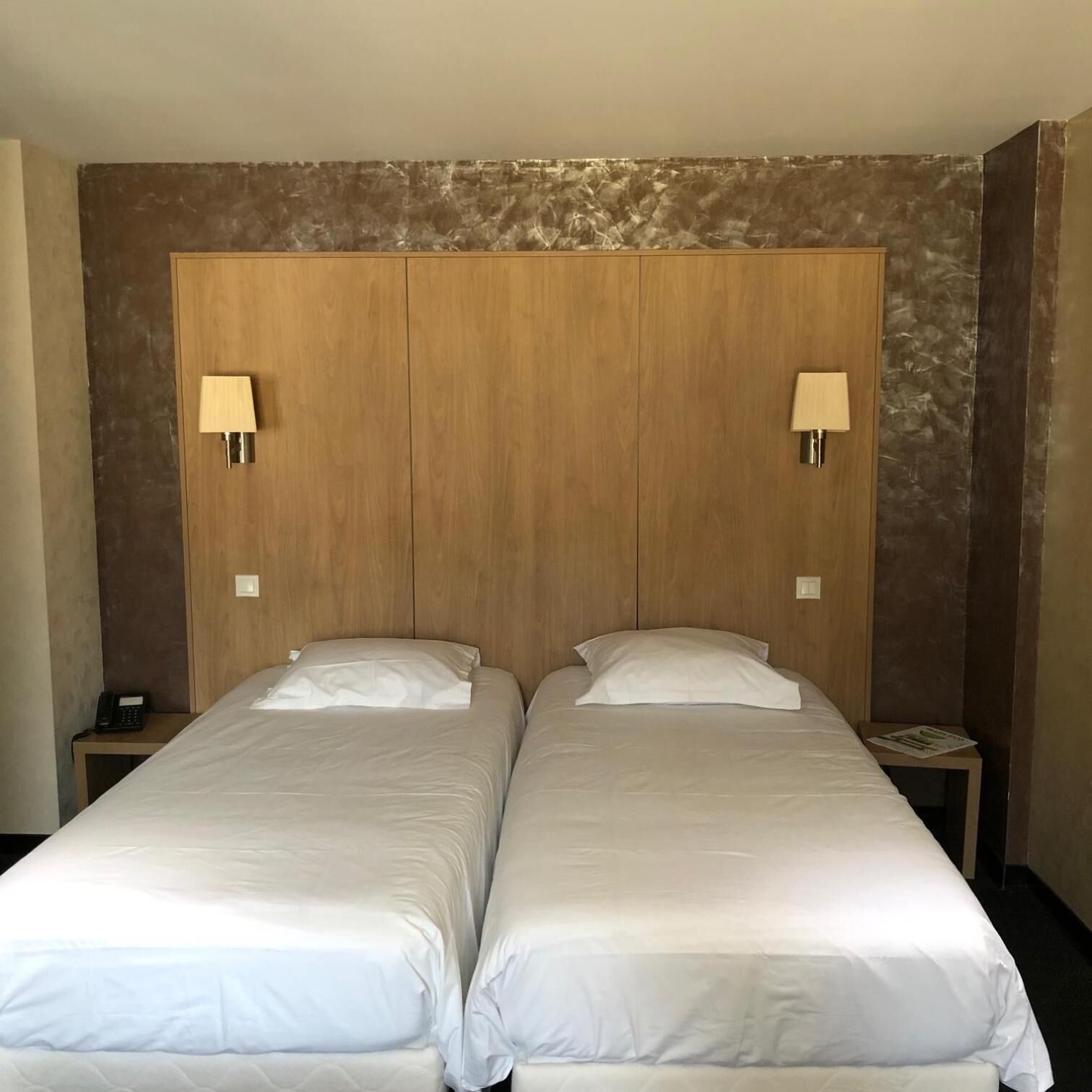 A double bed with a wooden headboard, two bedside lamps, and a small bedside table with a phone.