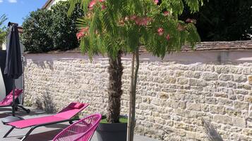 A patio area with a stone wall, a tree with pink flowers, and outdoor seating with a modern chair and a lounge chair.