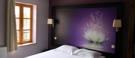 A bedroom with a bed, a window with curtains, a wall-mounted TV, and two wall lamps.
