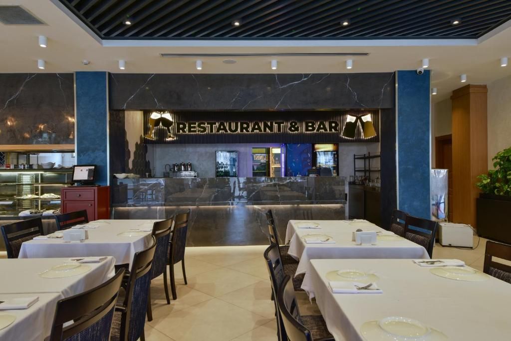Un restaurant avec des tables dressées pour le service, un coin bar et une cuisine en arrière-plan.