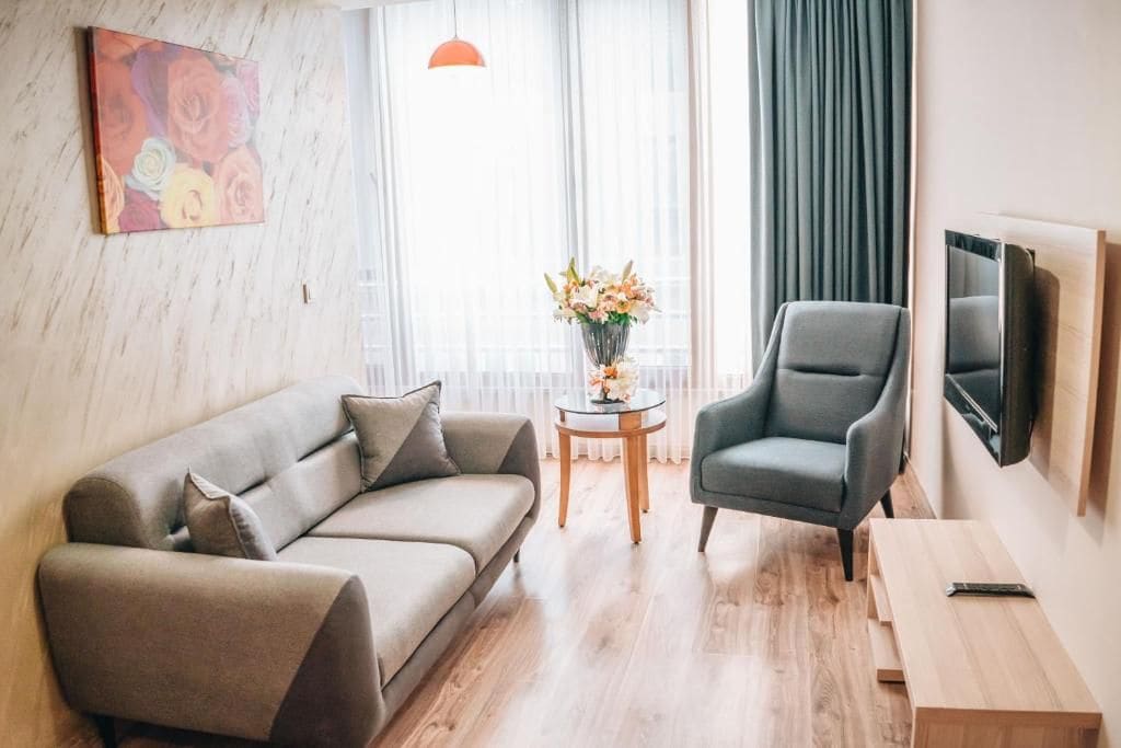 A modern living room with a sofa, armchair, small round table with flowers, and a television mounted on the wall.