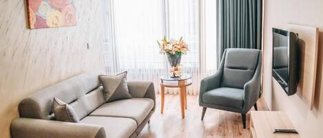 A modern living room with a sofa, armchair, small round table with flowers, and a television mounted on the wall.