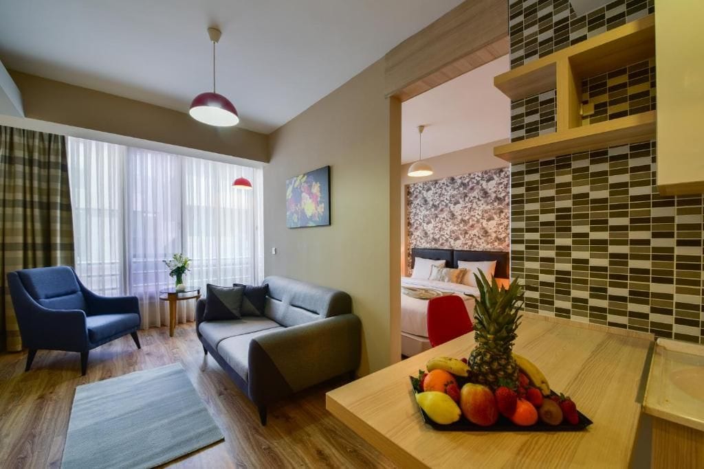A modern hotel room with a sofa, armchair, and a fruit bowl on the table.