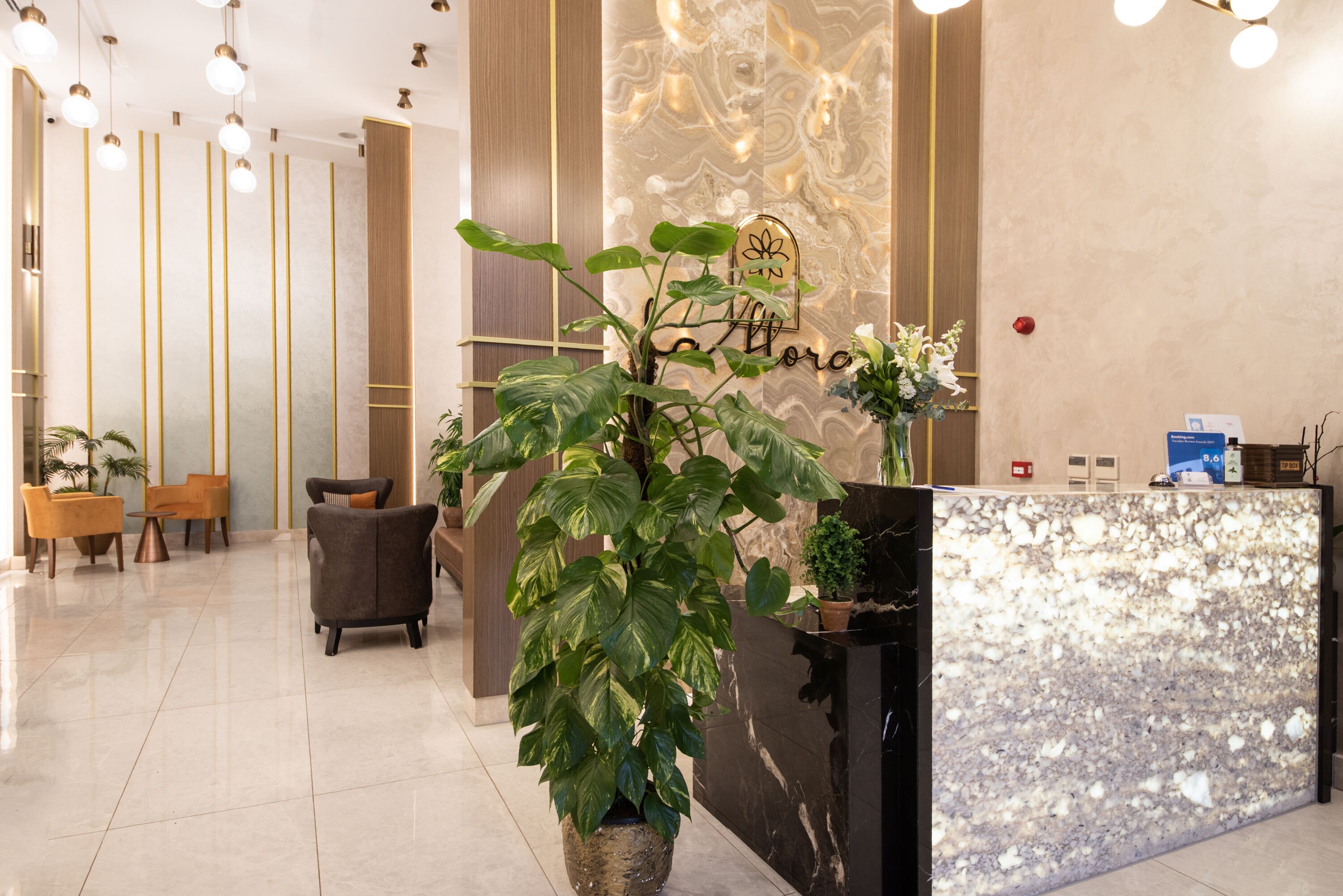 A modern reception area with a marble reception desk, a large potted plant, and a seating area with chairs and a table.