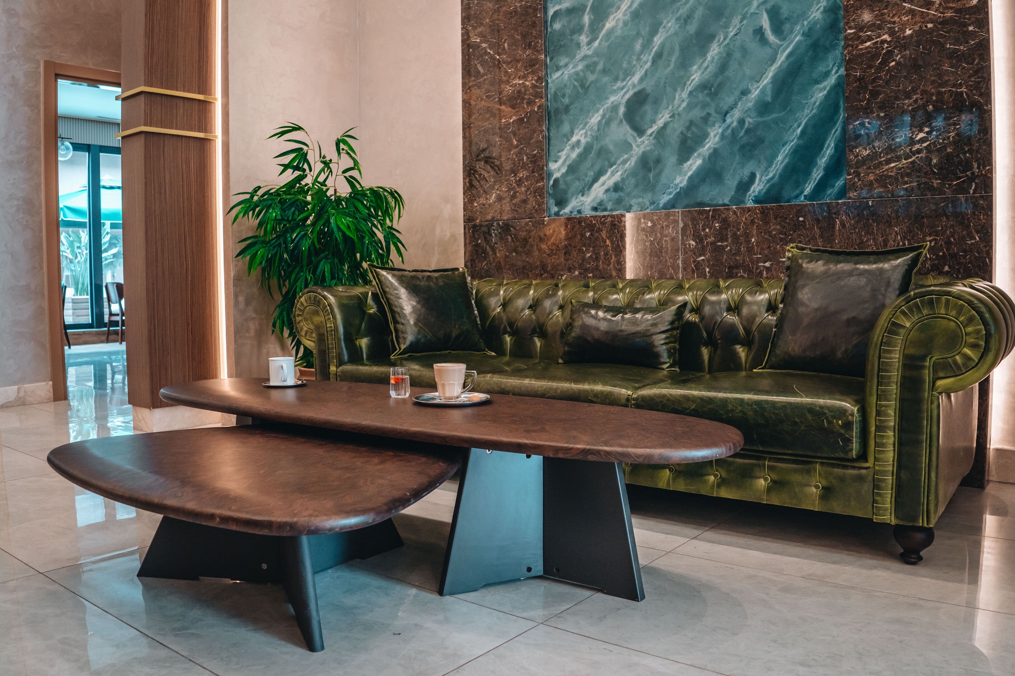 A modern lobby with a green velvet sofa, a wooden coffee table, and a large marble wall.