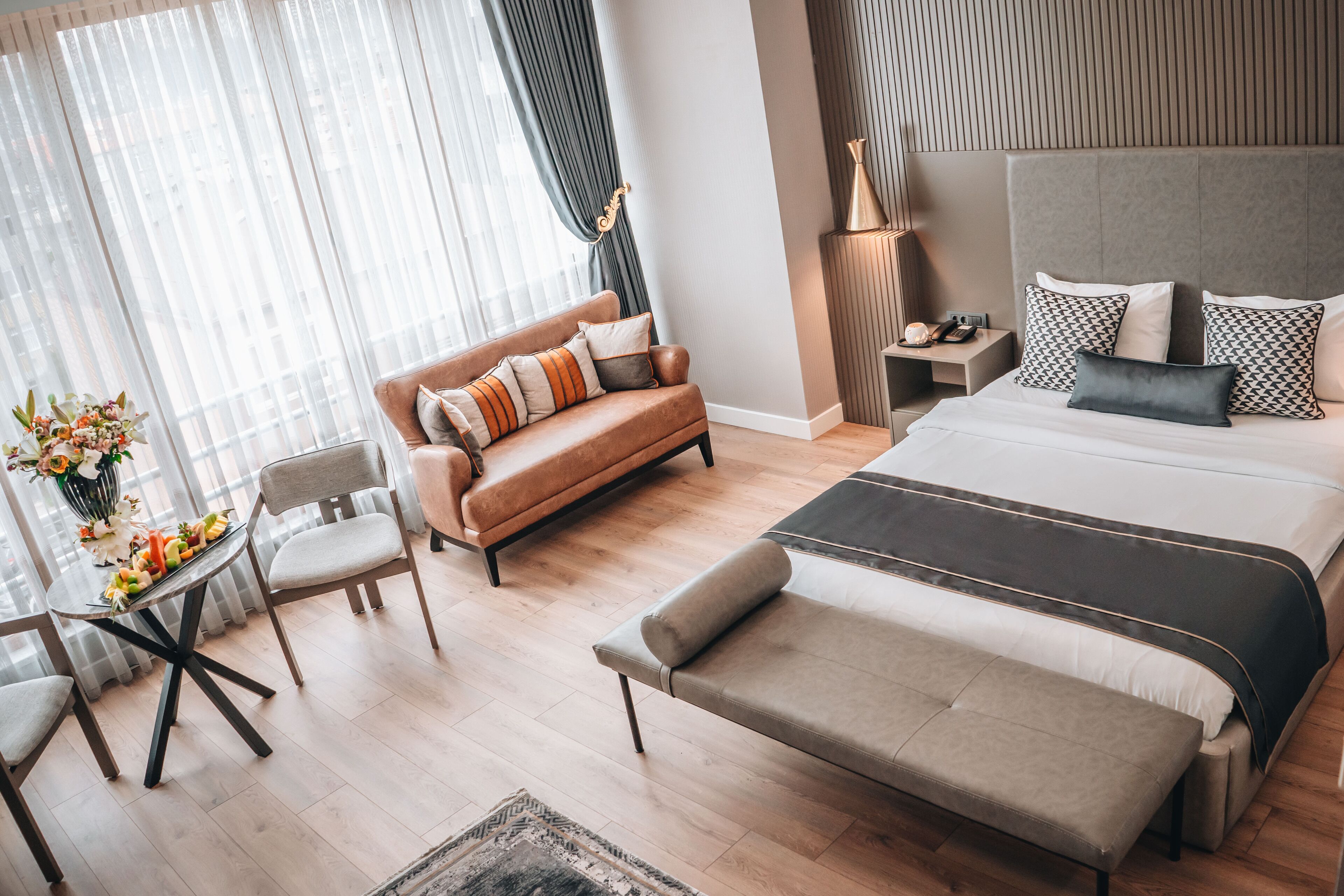 Een moderne hotelkamer met een groot bed, een bank, een eettafel met stoelen en een nachtkastje met een lamp.
