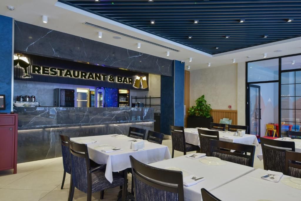 Un restaurant i bar amb taulells de marbre, teles de taula blanques i cadires de vimetla.