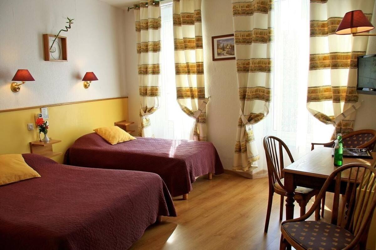 A hotel room with two beds, a wooden table, chairs, a TV, and curtains.